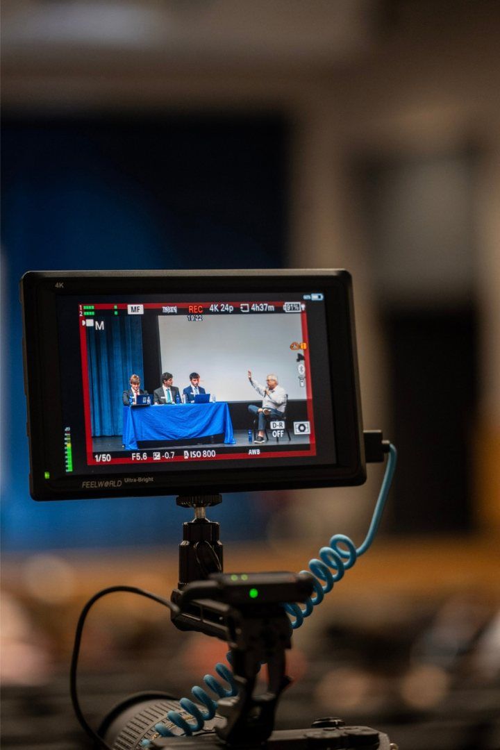 A camera monitor filming the panel from the back of the auditorium